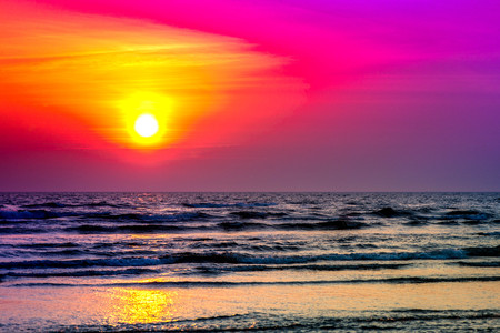 Golden, colorful, abstract sea sunset view at horizon, vibrant sky landscape and waves in the water. Sunrise reflection in nature with sun in clouds above black, dark ocean. Orange, blue, purple, red.の写真素材
