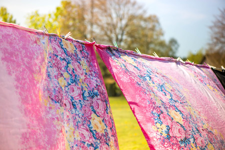 Holidays and vacation on countryside at camping. Just washed, fresh and aromatic cotton bed sheets and linen, hang out on a laundry line outside in the garden on a sunny summer day. A rural scene.の写真素材