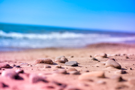 Macro shot of magical, healing, warm sea pebbles, stones and rocks, laying on beach sand. Ocean waves background in summer evening, during the sunset. Calm, relaxing walk on seaside. Perfect vacation.の写真素材
