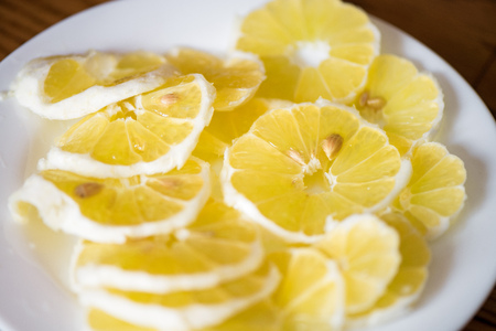 Shot of bright, yellow and sour lemon slices with seeds on white plate in the middle of table. Ready to be eaten or put in water glass and drinks.の写真素材