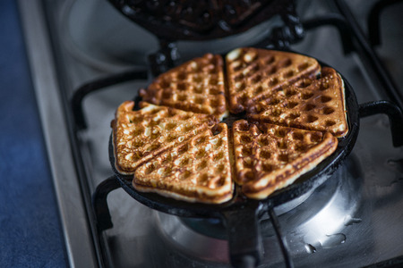 Macro shot of just cooked, delicious, tasty, hot yogurt pancakes with strawberry sauce on waffle iron on fire stove in kitchen. Dinner is ready. Sweet golden brown waffles with jam ready to be eatenの写真素材