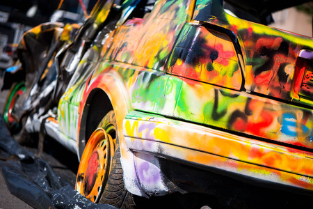 Macro shot of a colorfully painted car, an old crashed, damaged car wreck. Kids are having fun, making drawings and graffiti art, paint on wreck and tires with green, red, orange, yellow, blue colorsの写真素材