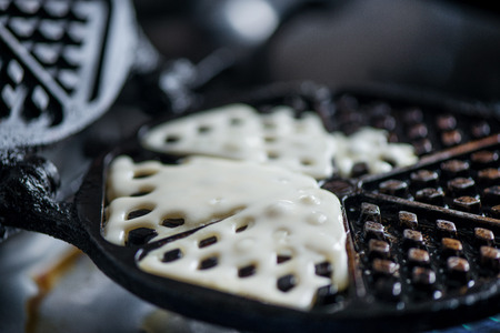 Macro shot of waffle dough being pour to hot waffle pan. Cooking yogurt pancakes with strawberry sauce on waffle iron on fire stove in kitchen. Dinner is ready. Sweet golden brown waffles with jam.の写真素材