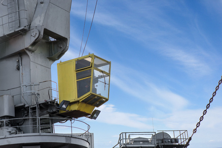 Shot of yellow control cabin with worker. Old, rusty, grey port crane lifting cargo in ship on clear blue sky background. Equipment for unloading ships and barges, preparing for export world wideの写真素材