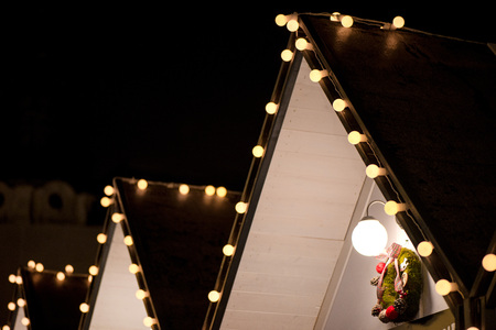 Crowded Christmas market in city center, decorated wooden huts with glowing lights. People enjoying event and searching for gifts. Beautiful Christmas background.の写真素材