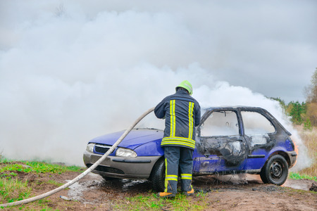 Fire fighter prepare to attack a propane fire. Burning and crashed car after explosion. Accident on street at countryside. No one was injured. Artificially created set for film makingの写真素材