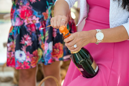 Girl in pink dress is opening champagne bottle to pour the drink in glasses. Cork is about to pop out. Cheerful bride and bridesmaids partyの写真素材
