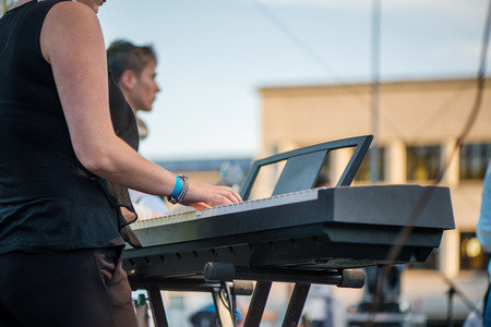 Male musician plays a musical instrument on the stage. Artist playing on the keyboard synthesizer piano keys. Live concert of choir music at night in summer festival. Colorful, abstract lightsの写真素材