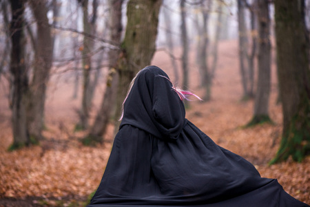 Girl in black hood running away from danger deep in dark forest. Thick fog all around. Scary autumn sceneの写真素材