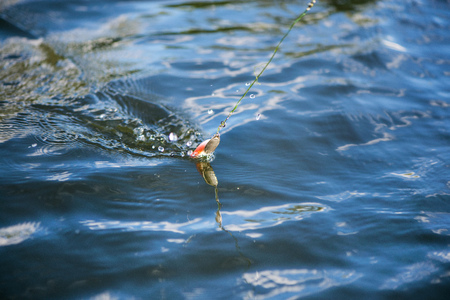 Plastic spinning bait catching fishes in water. Splashes, water drops around. Calm water background. Expensive fishing equipment. Favorite leisure activity for men at the weekendの写真素材