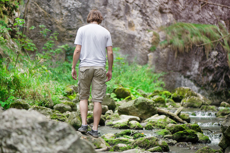 Young man relaxing by the river and looking in the sky. Small mountain stream with moss covered rocks deep in the forest. Cliffs in Cheile Turzii, Romania. Autumn is coming. Beautiful, calming natureの写真素材
