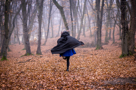 Girl in black hood running away from danger deep in dark forest. Thick fog all around. Scary autumn sceneの写真素材