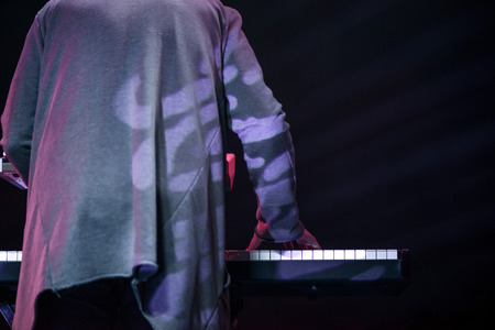 Male musician plays a musical instrument on the stage. Artist playing on the keyboard synthesizer piano keys. Live concert of electronic music at night in summer festival. Colorful, abstract lightsの写真素材
