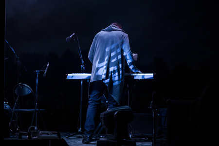 Male musician plays a musical instrument on the stage. Artist playing on the keyboard synthesizer piano keys. Live concert of electronic music at night in summer festival. Colorful, abstract lights.の写真素材