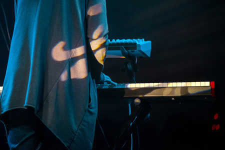 Male musician plays a musical instrument on the stage. Artist playing on the keyboard synthesizer piano keys. Live concert of electronic music at night in summer festival. Colorful, abstract lights.の写真素材