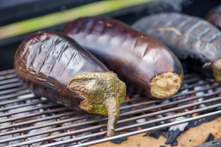 Aubergine on barbecue grill on hot charcoal and fire. Preparing healthy food on holiday. Cooking vegetables on flames. Delicious meal for vegetarians and vegansの写真素材