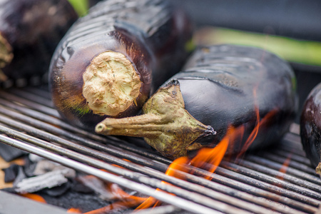 Aubergine on barbecue grill on hot charcoal and fire. Preparing healthy food on holiday. Cooking vegetables on flames. Delicious meal for vegetarians and vegansの写真素材