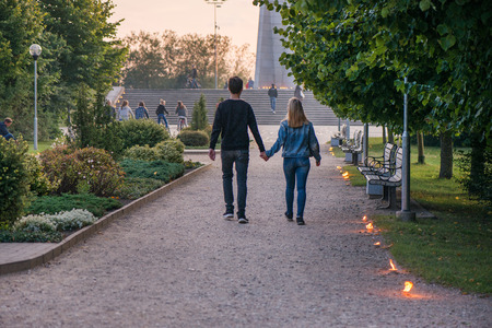 Happy couple holding hands and walking in park on lit candle path during sunset. Romantic summer evening, love is in the air. People celebrating Night of ancient lights. Calm and relaxing holidays.の写真素材
