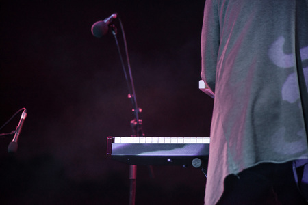 Male musician plays a musical instrument on the stage. Artist playing on the keyboard synthesizer piano keys. Live concert of electronic music at night in summer festival. Colorful, abstract lightsの写真素材