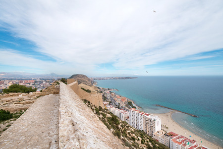 Panoramic view of Postiguet beach  from Santa Barbara Castle in Alicante, Spain. Sunny day at Mediterranean sea. Block apartment buildings in a row. Palm trees and vibrant blue waterの写真素材