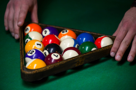 Sport billiard balls set arranged in shape of triangle on green billiard table in pub. Players are...