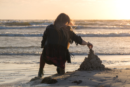 Young woman building and making sand castle next to sea. Calm, relaxing and romantic evening during sunset at the beach side. Remembering the childhood. Loneliness conceptの写真素材
