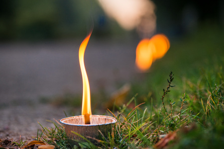 Macro shot of lit candle burning with soft glowing flame and smoke on evening background. Candle path at the park close to the seaside during the Night of ancient lightsの写真素材
