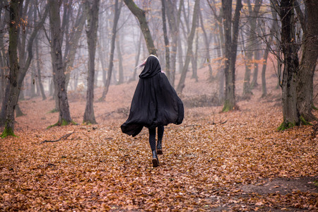 Girl in black hood running away from danger deep in dark forest. Thick fog all around. Scary autumn sceneの写真素材