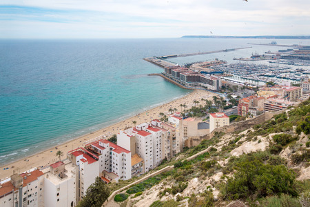 Panoramic view of Postiguet beach  from Santa Barbara Castle in Alicante, Spain. Sunny day at Mediterranean sea. Block apartment buildings in a row. Palm trees and vibrant blue water.の写真素材