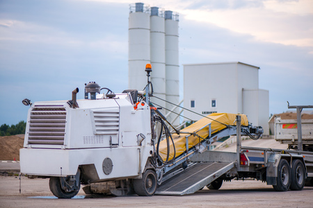 Cold milling machine being transported. Transportation trucks and construction machinery in large parking lot in industrial territory, next to concrete and asphalt factoryの写真素材