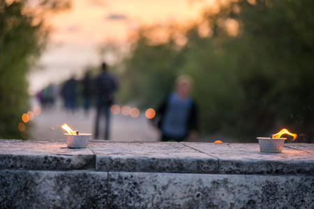 Macro shot of lit candle burning with soft glowing flame and smoke on romantic sunset background. Candle path at the park close to the seaside during the Night of ancient lightsの写真素材