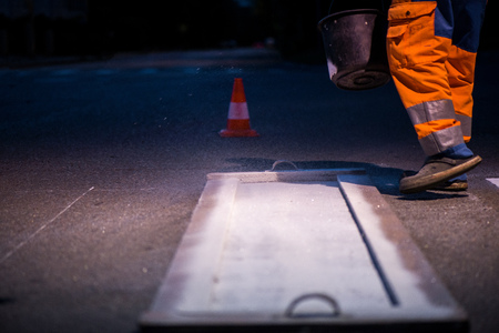 Traffic line painting. Workers are painting white street lines on pedestrian crossing. Road cones with orange and white stripes in background, standing on asphalt during road construction worksの写真素材