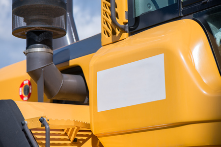 Space for text or logo. Side of yellow excavator. Road construction workers repairing highway road on sunny summer day. Loaders and trucks on newly made asphalt. Heavy machinery working on streetの写真素材