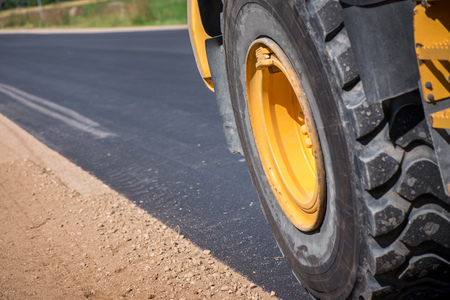 Macro shot of a wheel of loader truck during road construction works on side of highway. Freshly...