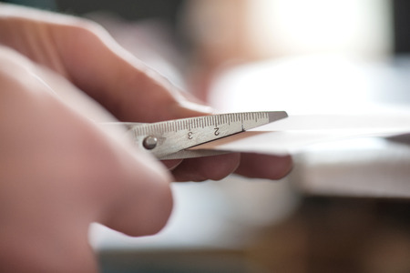 Macro shot of old scissors cutting white paper sheet in two partsの写真素材