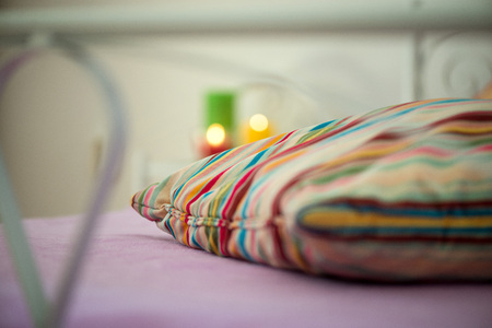 Macro shot of a colorful pillow taken through a modern design style bed. Warm light from lit candles in the background.の写真素材
