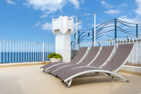 Four sunbathing beds layed on a villa roof next to the sea side. Beautiful view of blue sky and clean blue sea.の写真素材