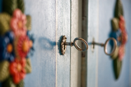 Decorative, vintage look ancient metal key in a blue, rustic doors in wardrobe keyhole. Beautiful flower ornaments. Concept of safety and secrets.の写真素材