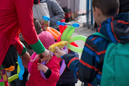 A freelance clown creating balloon animals and different shapes at outdoor festival in city center. School bag, angel wings, butterflies and dogs made of balloons. Concept of entertainment, birthdaysの写真素材