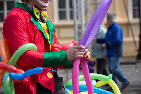 A freelance clown creating balloon animals and different shapes at outdoor festival in city center....