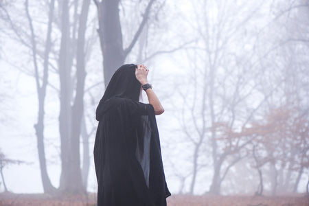 Girl in black hood standing on a stump deep in a dark forest. Waiting for magic to happen. Thick fog...