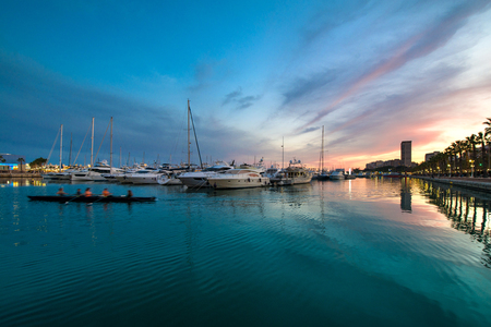 Beautiful port of Alicante, Spain at Mediterranean sea. Luxury yachts, ships, ferries and fishing boats sailing and standing in rows in harbor. Rich people traveling around the world. Sunset eveningの写真素材