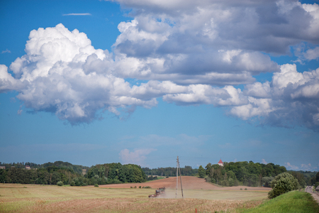 Agricultural background with red tractor pulling plow, throwing dust in air. Combine harvester at wheat field. Heavy machinery during cultivation, working on fields. Dramatic sky, rain, storm cloudsの写真素材