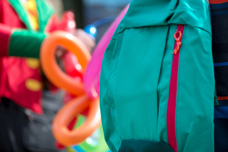 Close up shot of green school backpack. A freelance clown creating balloon animals and different shapes at outdoor festival in city center in the background. Concept of surveillance and stealingの写真素材