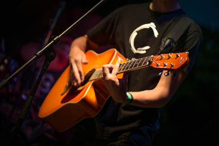 Macro shot of boy playing acoustic guitar on stage on evening. Band performing their songs. Music...