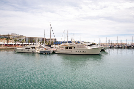 Beautiful port of Alicante, Spain at Mediterranean sea. Luxury yachts, ships, ferries and fishing boats sailing and standing in rows in harbor. Rich people traveling around the world. Sunny eveningの写真素材