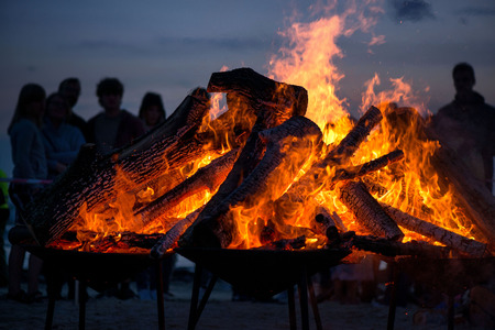 Large burning bonfire with soft glowing flame and sparkles flying all around. Romantic summer evening, people relaxing and enjoying calmness at the seaside during the Night of ancient lights.の写真素材