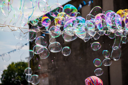 A freelance clown blowing hundreds of tiny, small and big bubbles at outdoor festival in city center. Concept of entertainment, birthdays. Kids having fun. Shower of bubbles flying in the happy crowdの写真素材