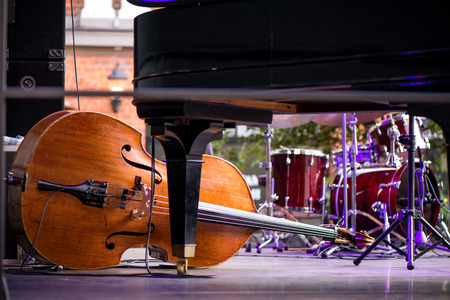 Wooden cello or violin on stage prepared for playing. Classical instruments, piano, drums in background.の写真素材