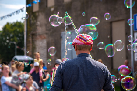Freelance clown blowing hundreds of tiny, small and big bubbles at outdoor festival in city center.の写真素材